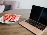 A laptop on a table with next to it a plate with slices of watermelon