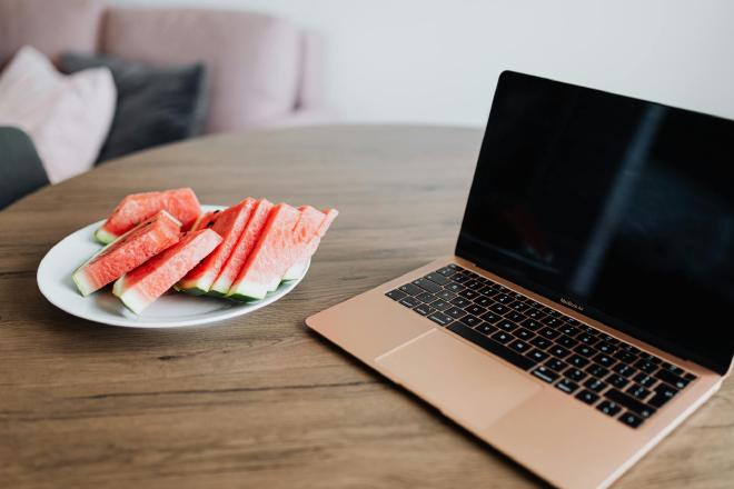 A laptop on a table with next to it a plate with slices of watermelon